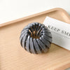 A silver-gray horsetail hair clip is displayed on a wooden tray next to a card.