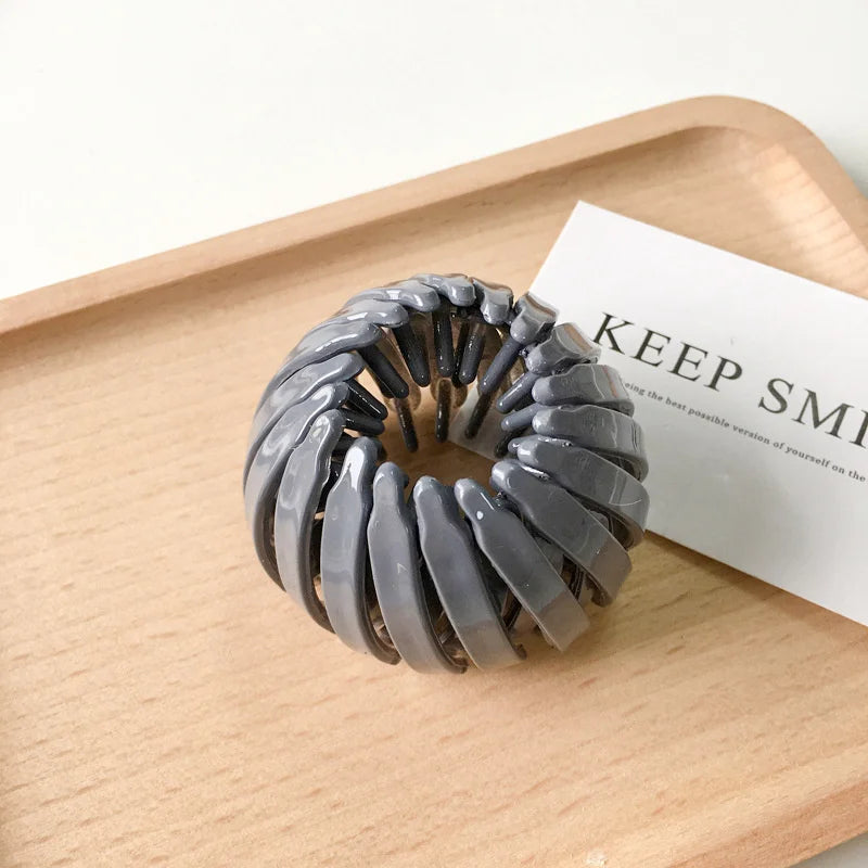A silver-gray horsetail hair clip is displayed on a wooden tray next to a card.