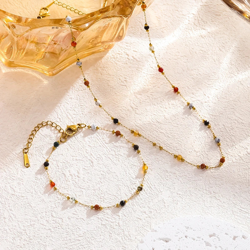 A delicate gold-toned beaded jewelry set with amber and dark colored beads displayed next to a translucent yellow bowl.