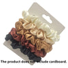 A set of five satin hair scrunchies in shades of beige, gold, rose, and black displayed on a white cardboard backing.