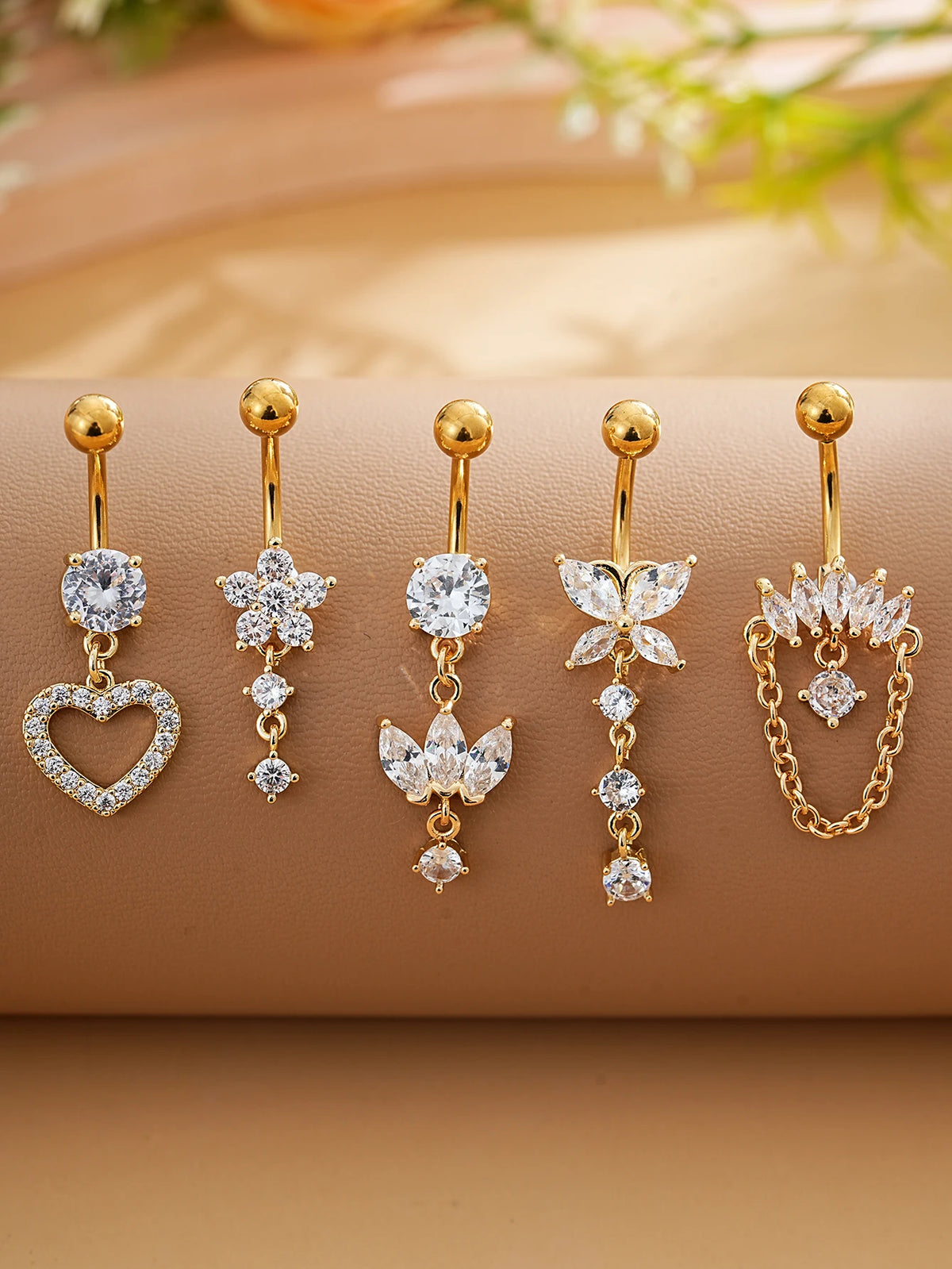 A set of five gold stainless steel dangled belly button rings featuring various diamond and floral designs.