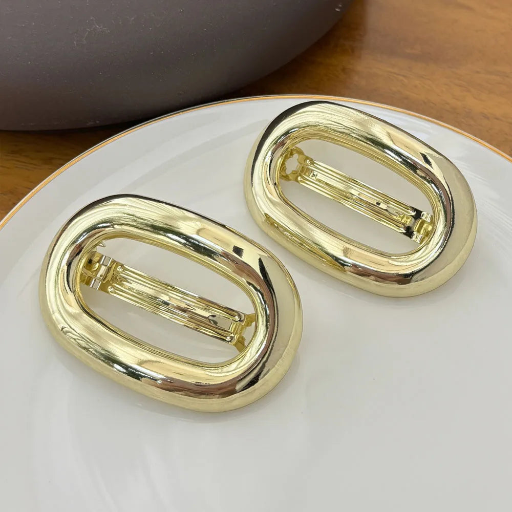 A pair of elegant gold metal oval hair clips resting on a white plate.