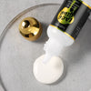 Eine Flasche Lace Glue Klebstoffspray mit weißer Applikator und goldener Kappe auf einer grauen Oberfläche.