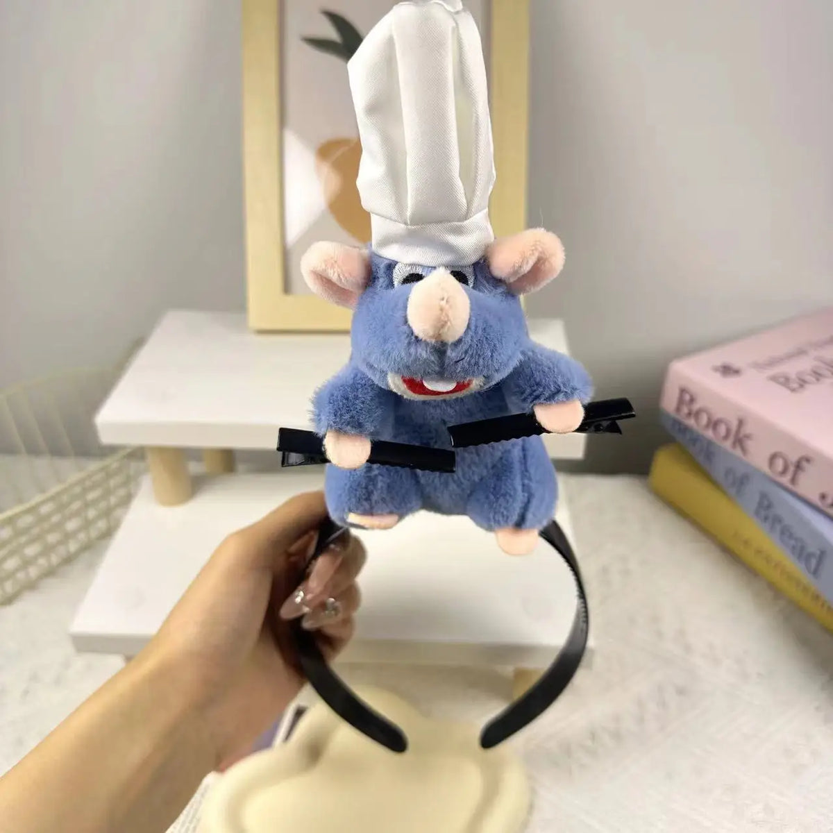 A blue plush mouse face hair accessory is being held up against a white background.