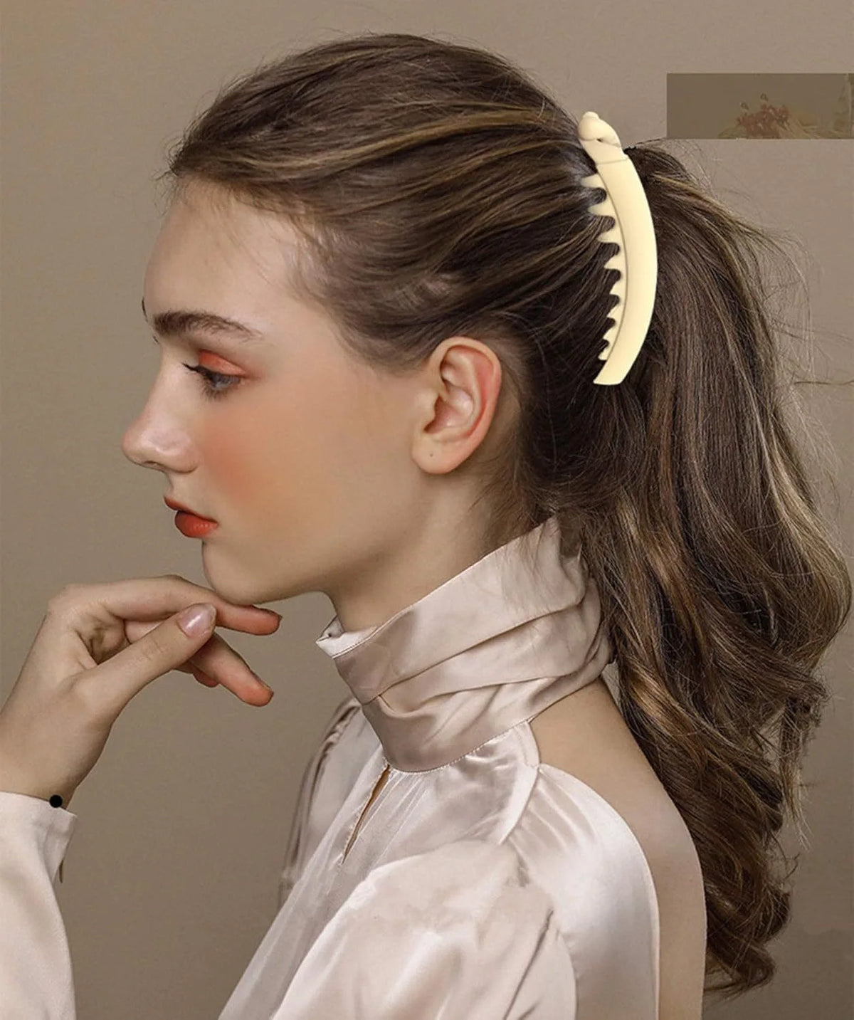 A close-up portrait of a woman with long brown hair styled in a ponytail, wearing a satin top and a large banana hair clip.