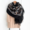 A black luxury floral scarf with beige trim and fringe draped over a light pink jacket.