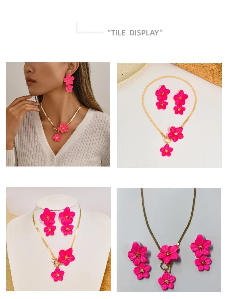 A gold-toned floral pendant necklace and matching earrings set featuring bright pink flowers.