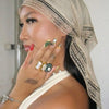 A woman wearing a beige bohemian lace trim shawl scarf, displaying various gold and silver rings on her hand.