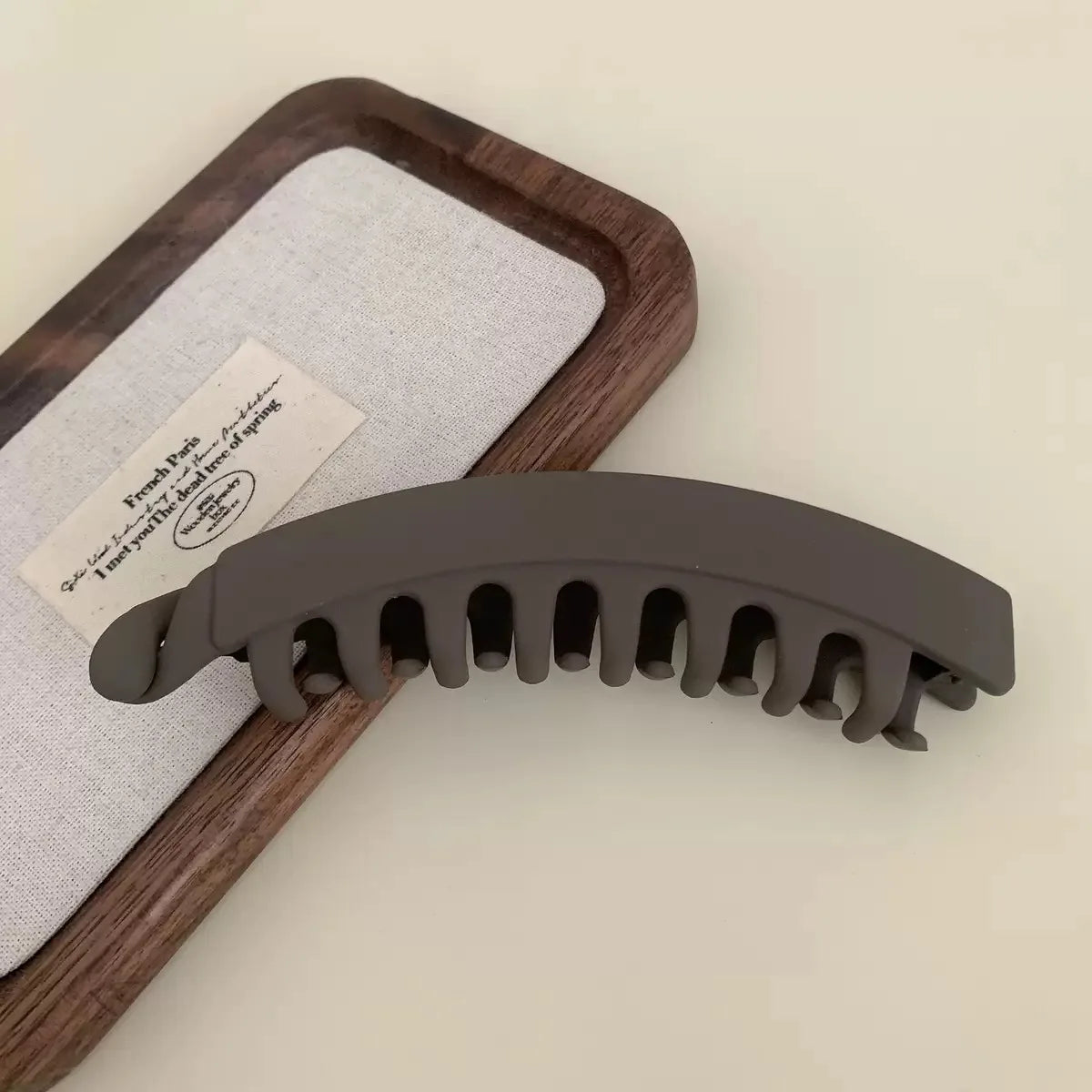 A set of large, dark gray banana hair clips resting on a wooden tray next to a white cloth.