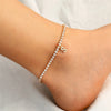 A gold-toned letter anklet bracelet with small clear stones worn on a person's ankle.
