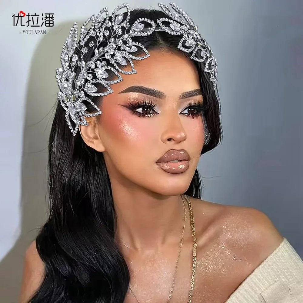 Model with silver rhinestone leaf bridal hairband and dramatic makeup against a gray background.