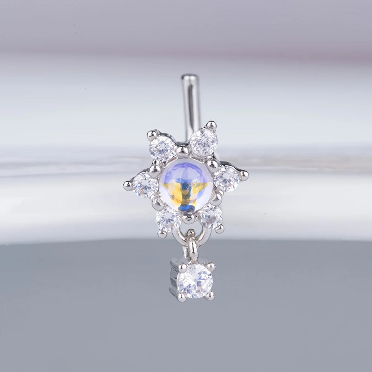Anneau nasal en acier inoxydable L argenté avec un cluster de petits diamants et une pierre bleue centrale.