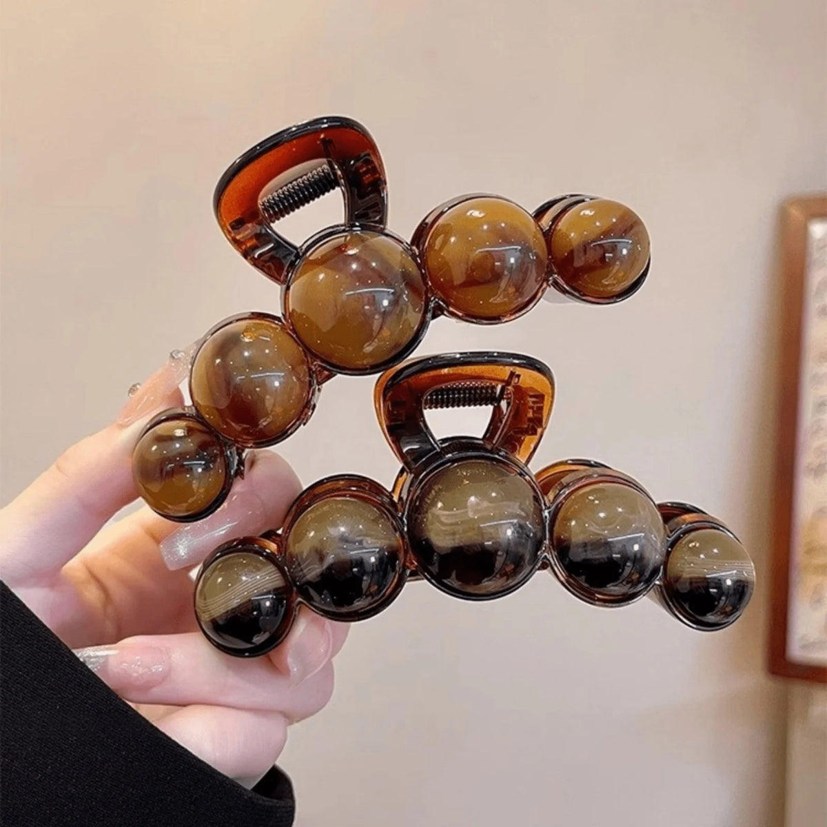 A hand holds an elegant acrylic pearl hair claw clip with amber and black tones.