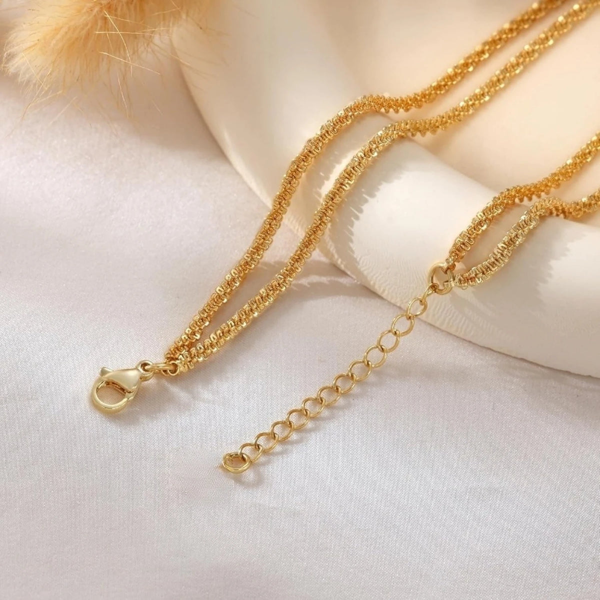 Gold silver plated adjustable beaded anklets draped on a white fabric with a feather detail