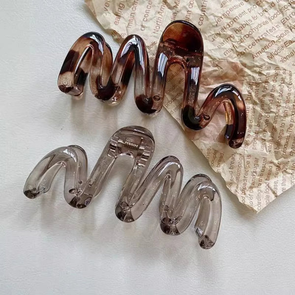 Dos pinzas para el cabello ámbar de alto brillo exhibidas sobre papel pergamino arrugado.