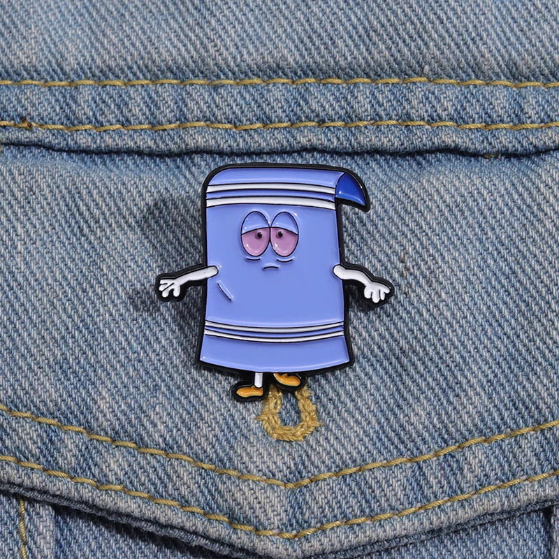 A purple cartoon towel enamel pin with wide eyes and a striped design pinned onto denim fabric.