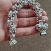 Eine Hand hält ein silbernes Totenkopf-Armband aus Vintage-Stil für Männer mit mehreren Totenkopf-Charms.