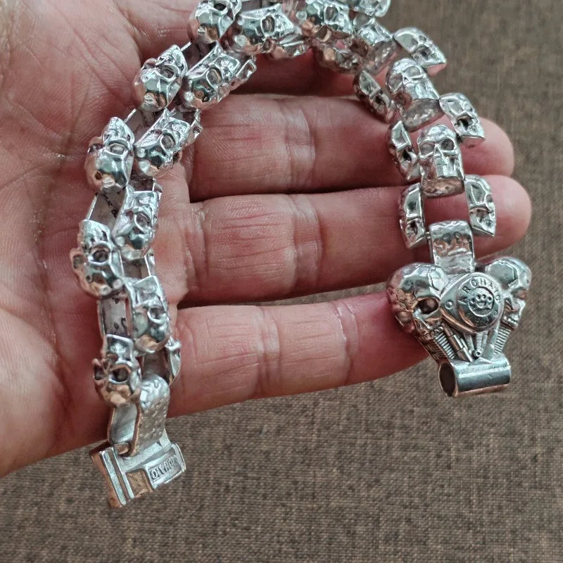 Eine Hand hält ein silbernes Totenkopf-Armband aus Vintage-Stil für Männer mit mehreren Totenkopf-Charms.