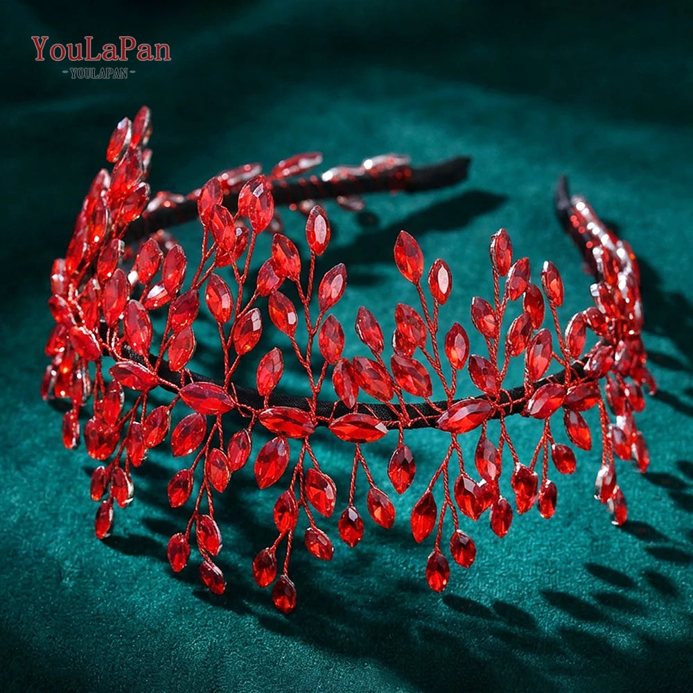 A close-up of a red rhinestone bridal headband with delicate floral accents resting on a dark green velvet surface.