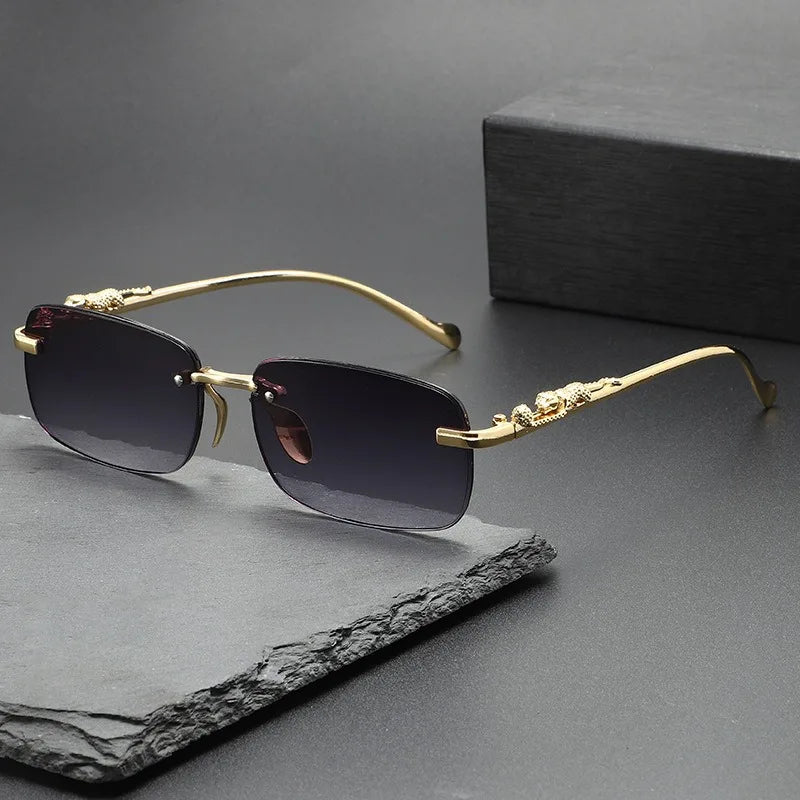 Gold-rimmed rimless square sunglasses resting on a dark gray slate surface.