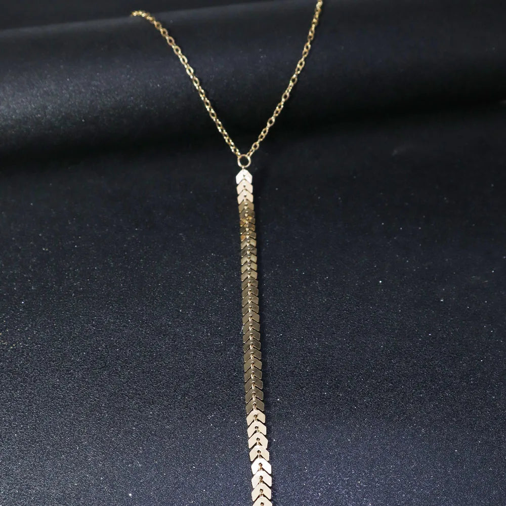 A gold minimalist wheat body chain necklace displayed against a dark background.