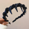 A dark blue resin wave toothed headband with spikes and textured surface being held by a hand.