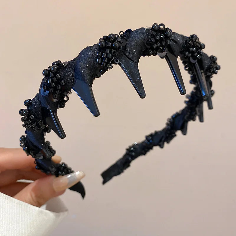 A dark blue resin wave toothed headband with spikes and textured surface being held by a hand.