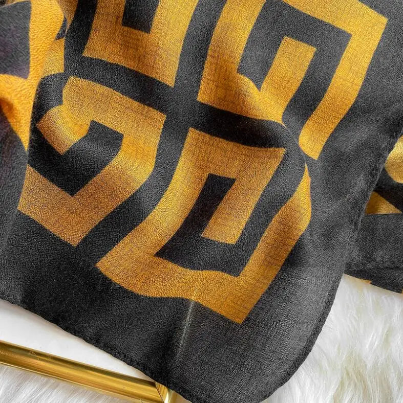 Nahaufnahme eines luxuriösen Baumwollpashmina-Schals mit geometrischem Muster in Gold und Schwarz.