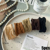 Five natural colored elastic hair bands for ponytails displayed on a white plate.