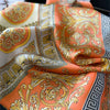 An orange and gold silk scarf with intricate baroque patterns folded on a dark surface.