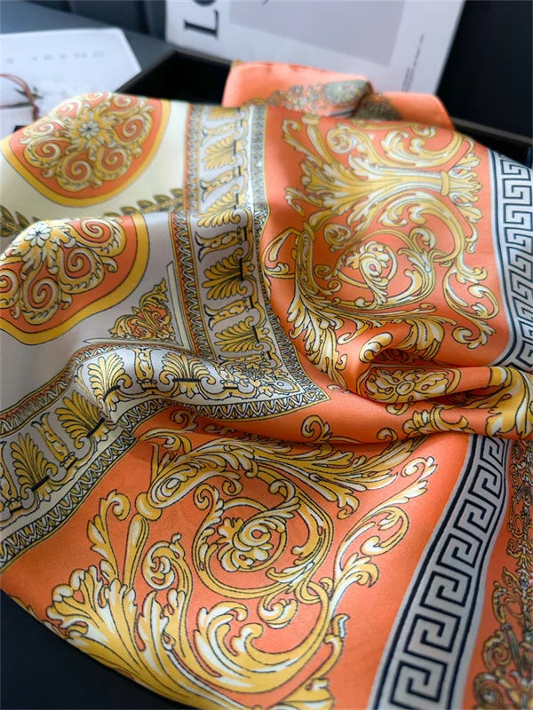 An orange and gold silk scarf with intricate baroque patterns folded on a dark surface.