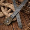 A dark leather belt with a floral engraving is laid across a thick rope on a wooden surface.