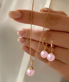 A hand models a dainty pearl jewelry set featuring matching earrings and a delicate necklace.