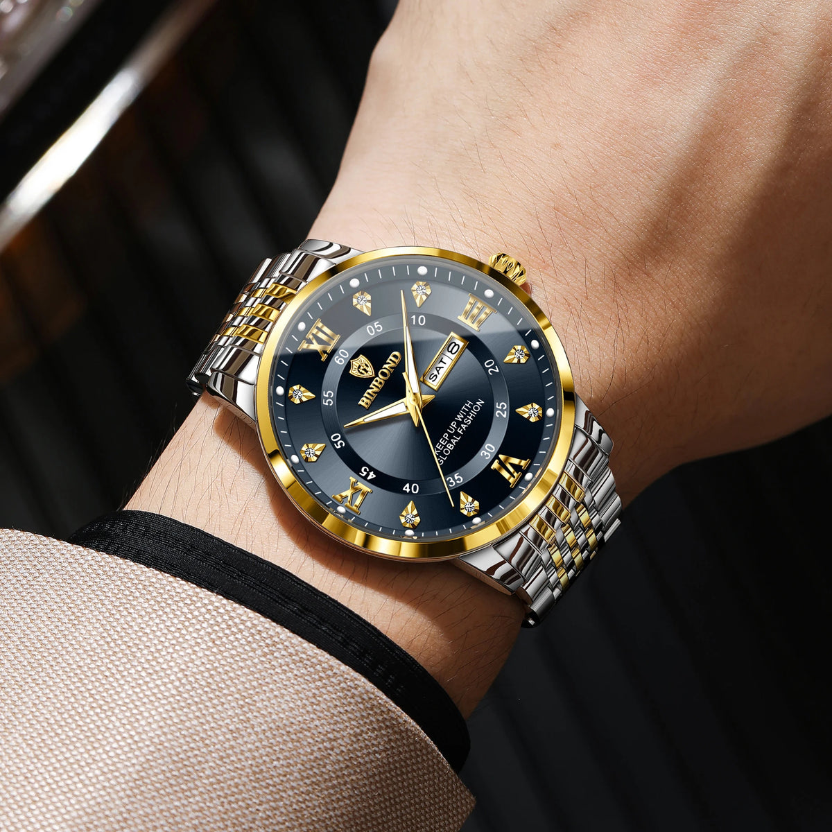 A close-up shot of a gold and silver luminous quartz wristwatch worn on a wrist against a dark background.