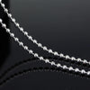 A close-up of a stainless steel pendant necklace with small silver beads, reflecting on a dark surface.