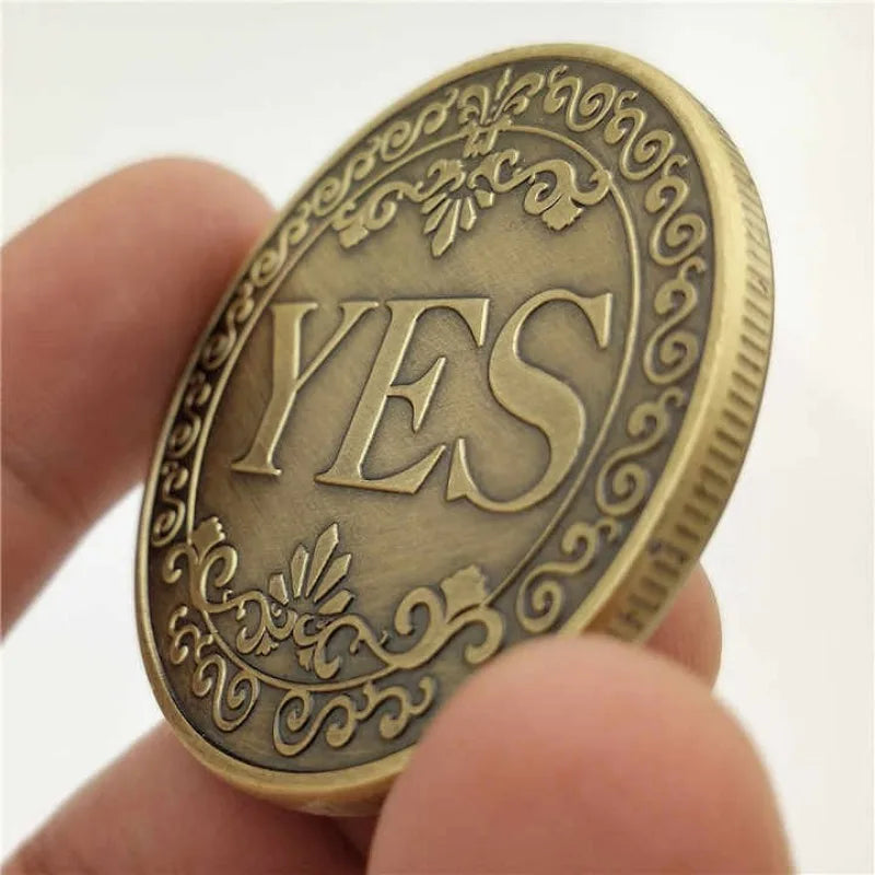 A close-up of a vintage antique bronze decision coin engraved with the word YES held between fingers.
