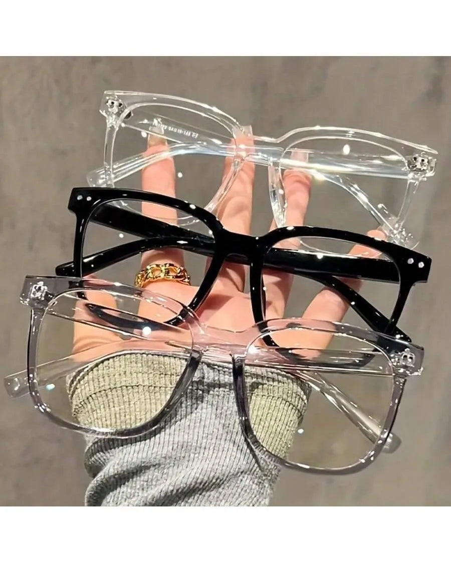 Una mano sostiene un paquete de tres gafas cuadradas transparentes y negras para bloquear la luz azul.