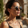 A woman wearing gold-rimmed sunglasses with crystal bead lanyards and chains.
