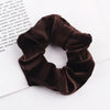A dark brown velvet scrunchie is shown resting on a white surface next to some printed text.