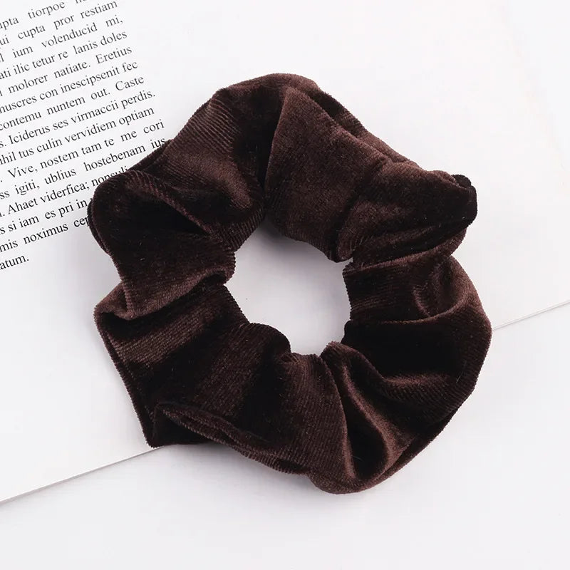 A dark brown velvet scrunchie is shown resting on a white surface next to some printed text.