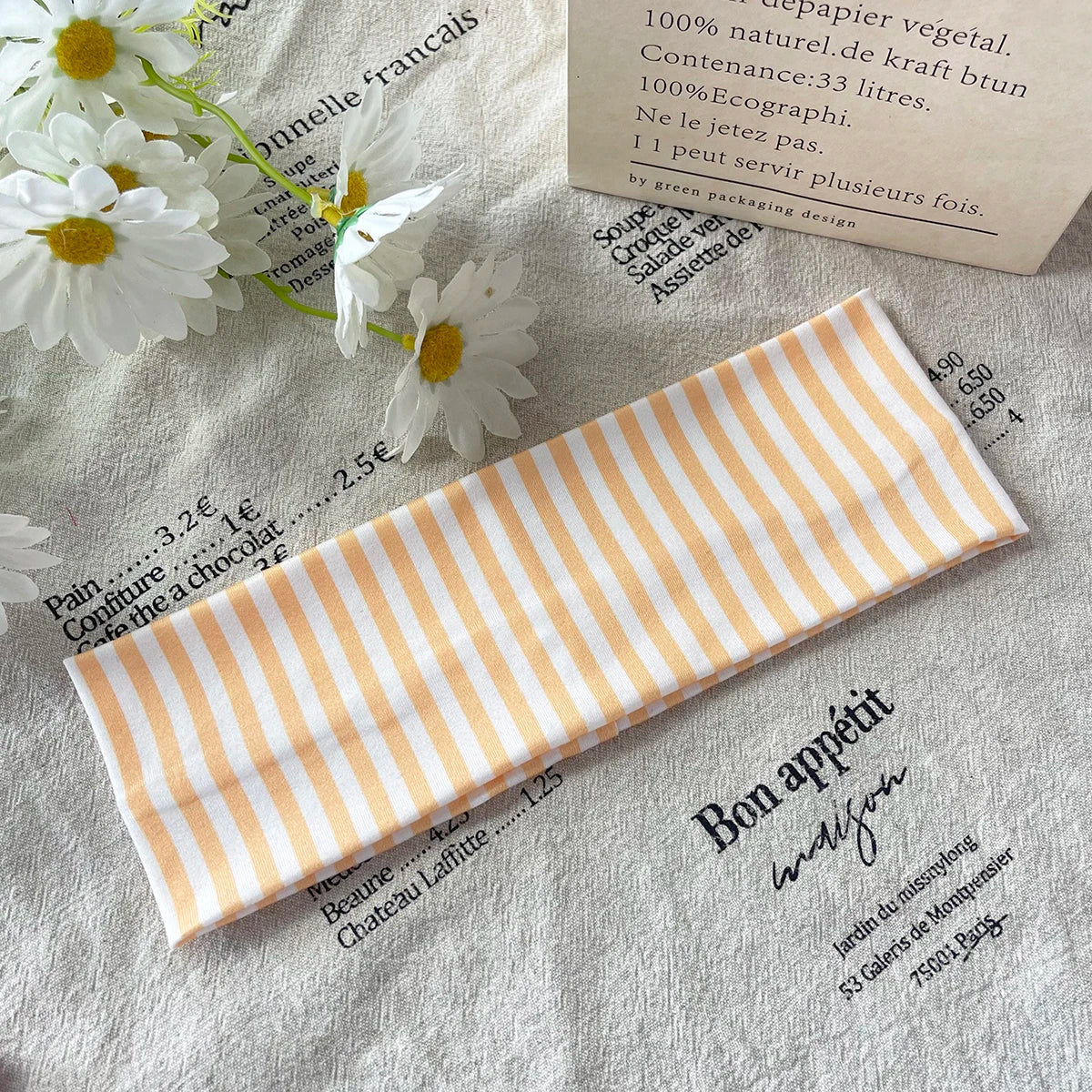 Un article en tissu rayé orange et blanc posé sur un tissu gris clair à côté de fleurs séchées.