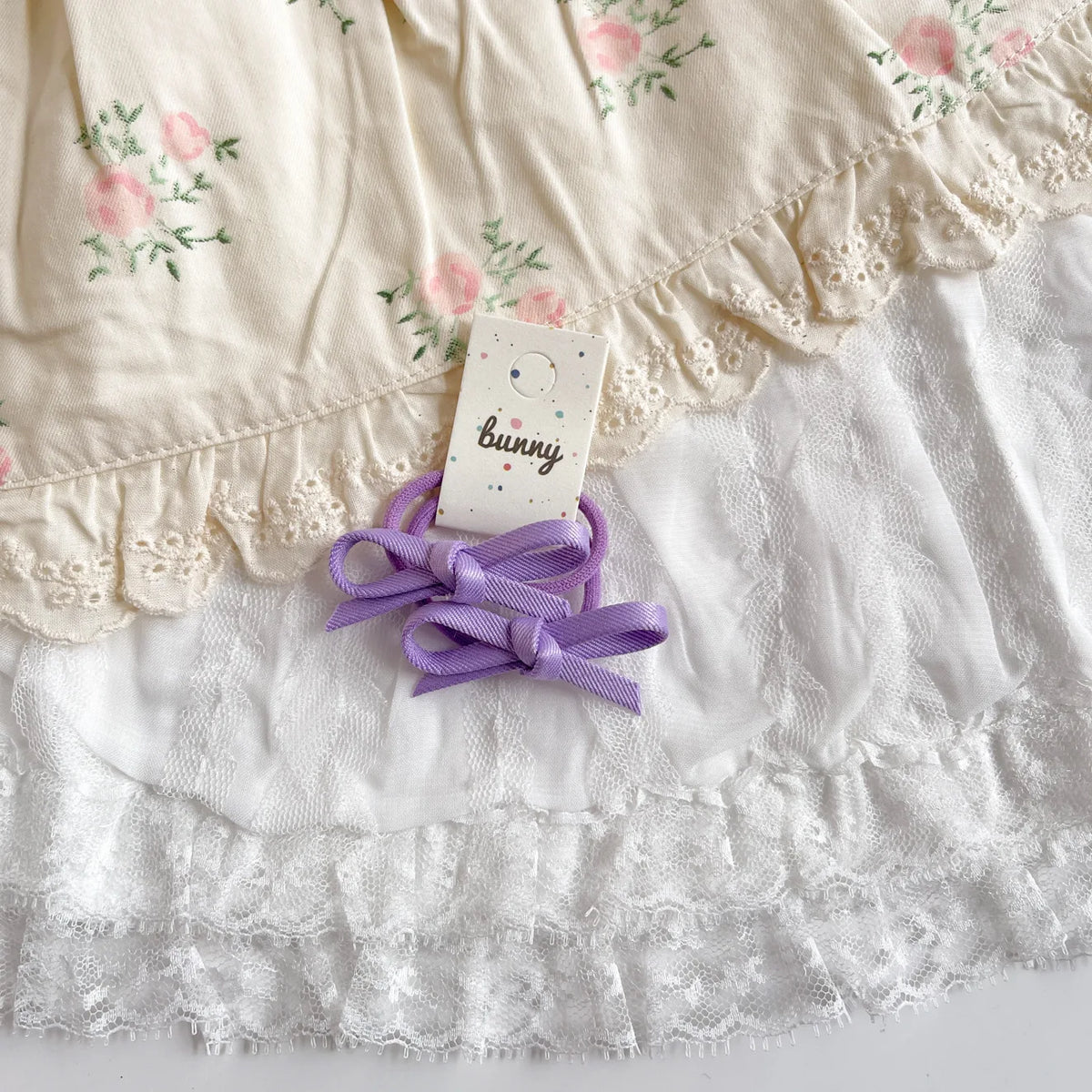 Un set de pinces à cheveux en nœud violet avec un motif lapin, posé sur du tissu en dentelle blanche.