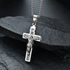 Colgante de cruz de Jesús en tono plateado con figura detallada, mostrado sobre una superficie de piedra oscura.