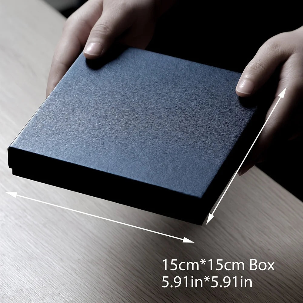 A hand holds a dark blue square box with white measurement lines on a wooden surface.