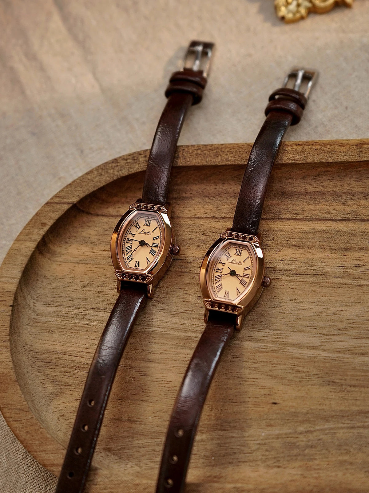 Reloj de correa de cuero marrón con caja de oro rosado y detalles decorativos sobre una tabla de cortar de madera.