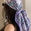 A woman wearing a purple and white floral satin shawl tied around her head, viewed from the back.