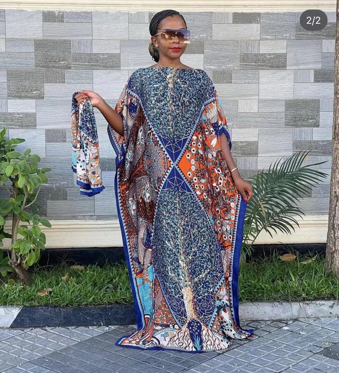 Eine Frau modelliert ein farbiges, bohémisches Seidenkleid mit Druck im Freien vor einer strukturierten Wand.