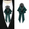 A dark green velvet bow tie with a silver rhinestone pendant worn on a white shirt and black suit jacket.