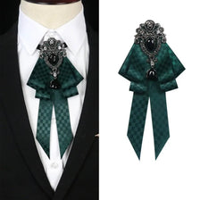A dark green velvet bow tie with a silver rhinestone pendant worn on a white shirt and black suit jacket.