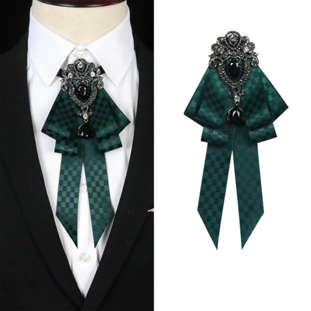 A dark green velvet bow tie with a silver rhinestone pendant worn on a white shirt and black suit jacket.